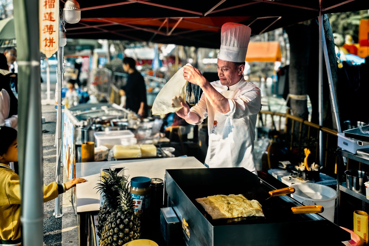 our-journey-03 Chef in Shenzhen street market making traditional Chinese crepes at an outdoor stall.