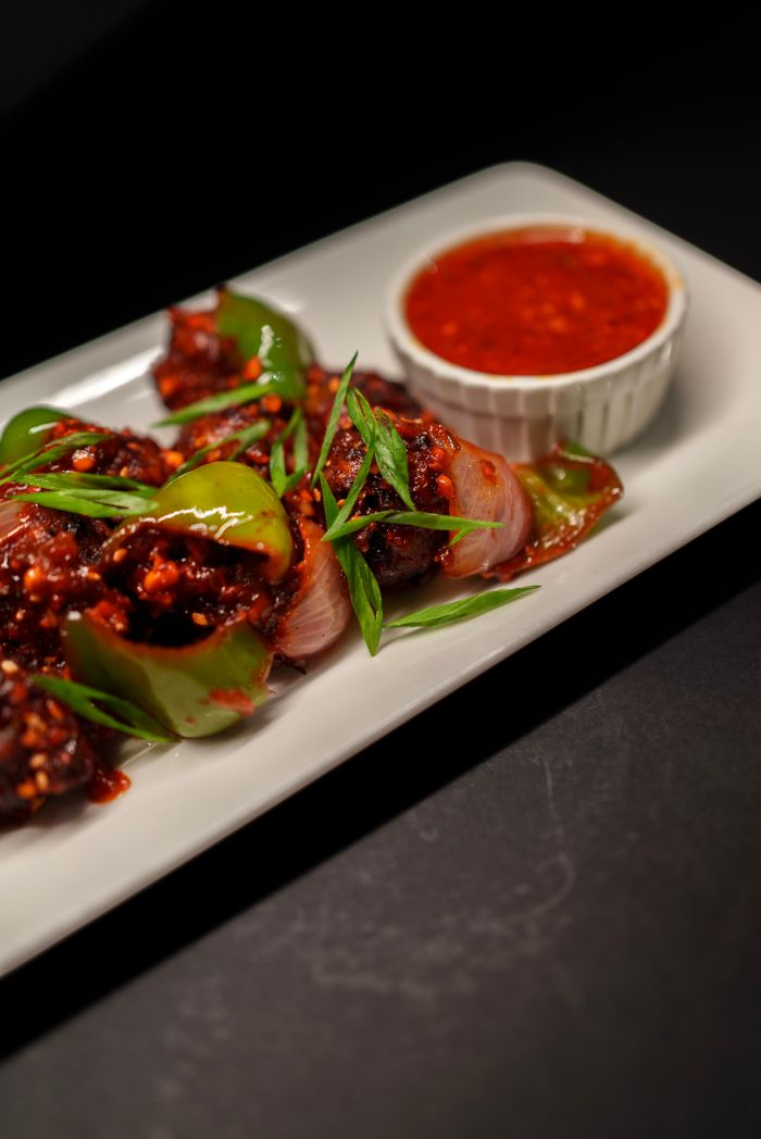 why-choose-us Close-up of spicy Indo-Chinese chilli chicken with sauce, garnished with spring onions.