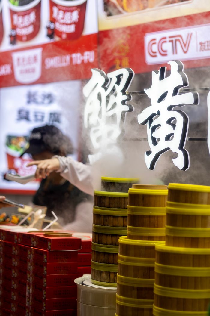 who-we-are Street vendor preparing food with steaming bamboo baskets in an Asian market setting.